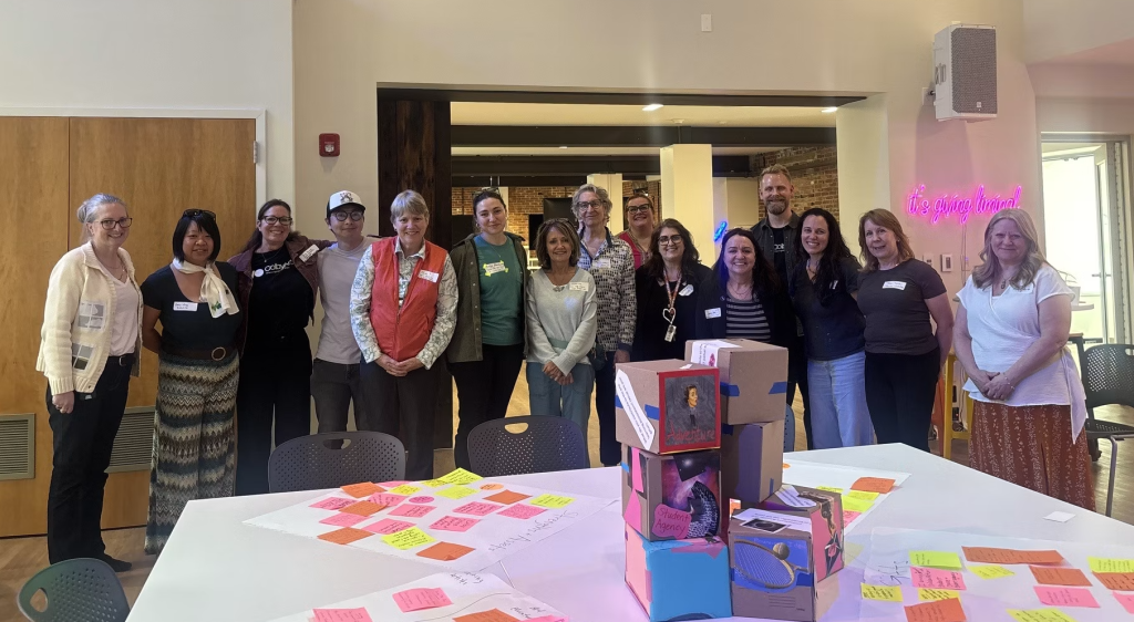 A group of adults standing in a line in front of artistic looking cardboard boxes.